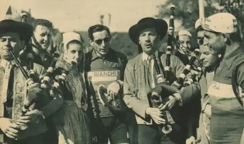 Photo en noir et blanc montrant deux hommes jouant d'un instrument de musique, à leurs côtés des coureurs cyclistes et une femme portant une coiffe blanche