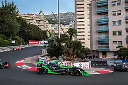 Photographie d'une monoplace verte et noire, vue de profil, dans une épingle, tournant à gauche, dans son ensemble.