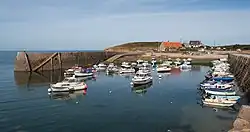Vue d'un petit port à marée haute. Une jetée sur la gauche, une quarantaine de petits bateaux de pêche et de plaisance au mouillage.