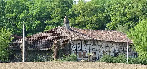 Un long bâtiment à colombages entouré d'arbres, surmonté d'une cheminée sarrasine ressemblant à une petite tourelle.