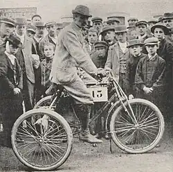 Photo d'un homme en tenue de ville sur un vélo portant un numéro à l'occasion d'une course.