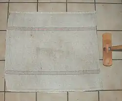 Un morceau de tissu en coton épais blanchâtre agrémenté de fines lignes colorées et une sorte de balais sans poils.