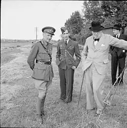 Sur fond de paysage de campagne, le général Montgomery (âgé d'une cinquantaine d'années, en uniforme) et Winston Churchill (une soixantaine d'années, en civil) entourent Pierre II (âgé d'environ 18 ans, en uniforme).