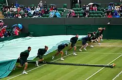 Une bâche en train d'être dépliée sur un terrain pour le protéger de la pluie