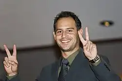 Plan poitrine d'un homme de 36 ans souriant de toutes ses dents en faisant le V de la victoire