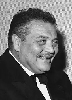 Photo en noir et blanc d'un cinquantenaire costaud en smoking, souriant.