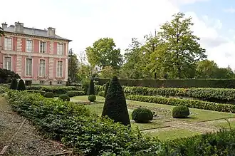 Le jardin clos Art déco vu légèrement de côté avec la Folie en arrière-plan à gauche. À gauche (1er&nbsp;plan) une allée décorée de briques, au centre une pelouse entouré de buissons taillés.