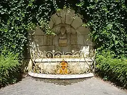  Fontaine surmontée d'un buste et entourée d’une balustrade dorée.