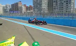 Photographie d'une monoplace de Formule E noire, dans les stands, sous un grand ciel bleu.