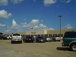 Vue partielle de la façade d'un long bâtiment masqué par différents véhicules sur le parking.