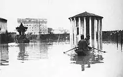 Photographie en noir et blanc représentant une barque sur une place inondée.