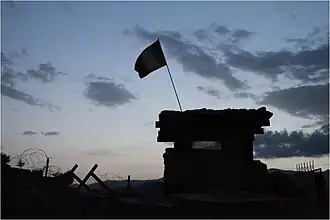 Un drapeau flotte au-dessus d'un tour militaire devant un ciel sombre.
