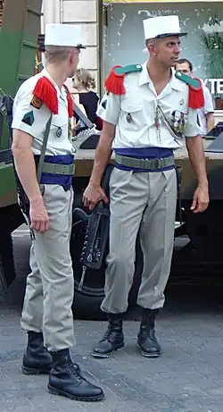 Soldats de la Légion étrangère en uniforme de parade. Épaulettes rouges à parement vert, ceinture bleue et képi blanc distinctif.