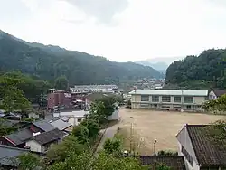 Photo couleur d'un village entouré de forêts sous un ciel nuageux.