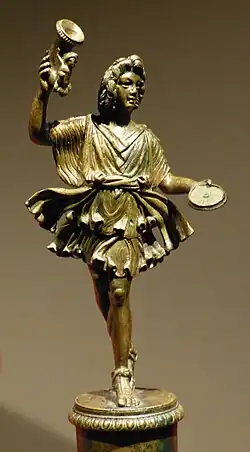 Statue: homme debout, jambes croisées, avec corne à boire & assiette, court vêtu, jupe flottante pour un effet dansant.
