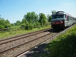 Passage d'un train près du quai de l'ancienne gare, par temps ensoleillé.