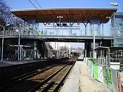 Photographie couleur. Voies et quais enjambés par une passerelle. Sur un quai : barrières de chantier.