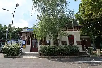 Photographie en couleurs d'un bâtiment d'un étage mansardé, au milieu d'arbres, avec une petite place devant.