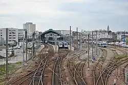 Vue d'ensemble du faisceau des voies de la gare, avec des trains et la verrière ; en arrière-plan, à droite, l'église Saint Joseph.