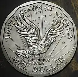 Pièce de monnaie représentant un aigle volant devant le soleil levant, treize étoiles et les inscriptions United States of America, One Dollar et E Pluribus Unum.