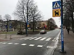 passage piéton ; à côté se situe un poteau avec un panneau représentant la silhouette du bouc en noir sur fond jaune.