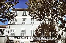 Contre-plongée sur un bâtiment de style provençal de trois étages, à l'ombre de platanes. Sur la façade l'inscription « Gendarmerie nationale ».