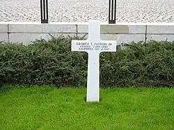 Simple croix blanche au milieu de l'herbe devant un petit muret