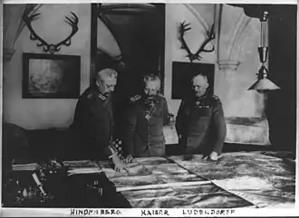 Le général Paul von Hindenburg, l'empereur Guillaume II et le général Erich Ludendorff, debout à une table, examinant de grandes cartes.