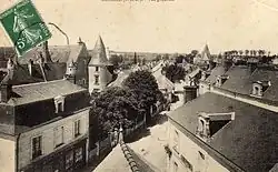 Vue d'un bourg prise d'un point haut, rue et maisons en contrebas, église en arrière plan.