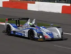 Photographie d'une voiture de sport-prototype, noire, bleue et grise, vue de trois-quarts avant, sur une piste