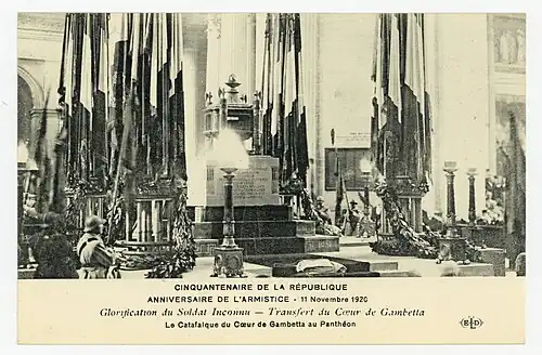 Carte postale ancienne en noir et blanc montrant un catafalque richement décoré entouré de drapeaux en bernes.