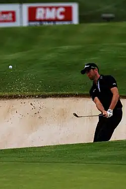 Un golfeur club en main jouant depuis le sable.