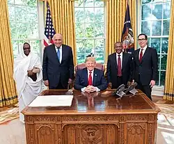 Homme assis à un bureau entouré par cinq personnes debout