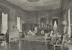 Photographie en noir et blanc d'un intérieur comportant des meubles et avec des boiseries sur les murs