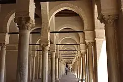Vue intérieure du portique occidental, montrant une succession d'arcades. Celles-ci sont soutenues par des colonnes à chapiteaux de styles différents.