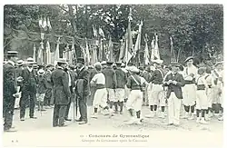 Photographie d'une foule parmi lesquels des groupes de gymnastes et des hommes portant des chapeaux, de nombreux drapeaux et bannières brandis en arrière-plan.