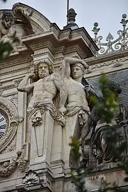 Termes de Jupiter et compagnon, Lyon, palais de la Bourse, horloge du fronton, façade nord.