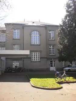 Bâtiment gris sur trois niveaux. La travée centrale forme un avant-corps.