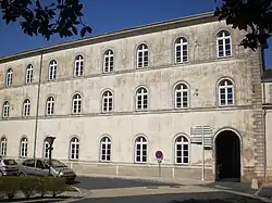 Façade de trois niveaux, les fenêtres blanches sont cintrées ; en bas à gauche, une porte noire, cintrée également.