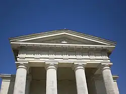 Le fronton triangulaire, la frise sculptée et les colonnes qui les supportent sont en pierre blanche.