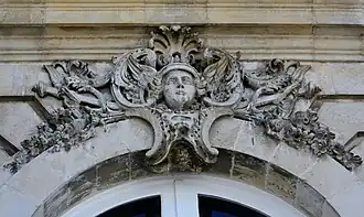 Mascaron ornant le dessus d'une fenêtre et figurant le dieu Hermès avec plusieurs attributs : pétase ailé, et deux caducée
