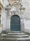 porte en bois à deux battants sous une arche portée par des pilastres. Le dessus est surmonté d'un fronton.