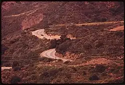 Vue aérienne de la route, entre les monts. Le tracé est très courbé.