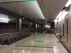 L'image laisse deviner sur le côté un escalator pour se rendre au niveau du quai de la station. Le sol est en carrelage.