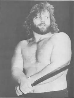 Une photo en noir et blanc d'un catcheur barbu torse nu aux cheveux long