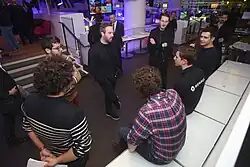 Photographie de plusieurs hommes en rond, discutant. La plupart sont debout, d'autres assis.