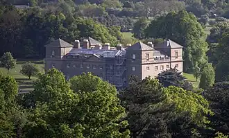 Photo. Vaste bâtiment rectangulaire, avec tours carrées, le tout dans un parc arboré