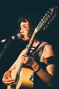 Photographie de la chanteuse Haley Heynderickx sur scène, chantant dans un micro et jouant de la guitare.