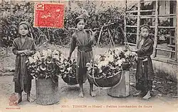 Trois petites filles asiatiques d'une dizaine d'années, en habit traditionnel, portant des grands paniers remplis de fleurs.