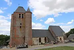 Vue latérale de l'église. À droite, le chœur et au centre , la nef, au toit surbaissé, en pierre calcaire, sont les parties les plus anciennes de l'église. Le donjon, entièrement en brique, a été construit au XVIIè siècle.